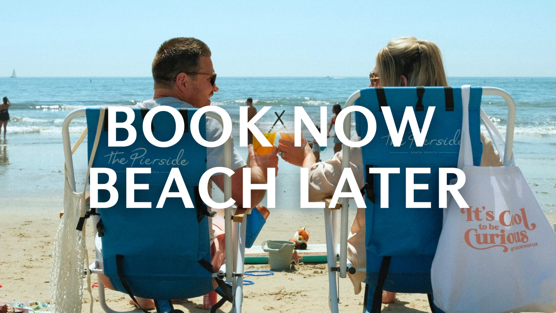 Beach scene with two people seated in blue lounge chairs on the sand, bold 'BOOK NOW BEACH LATER' text overlaid across the image.