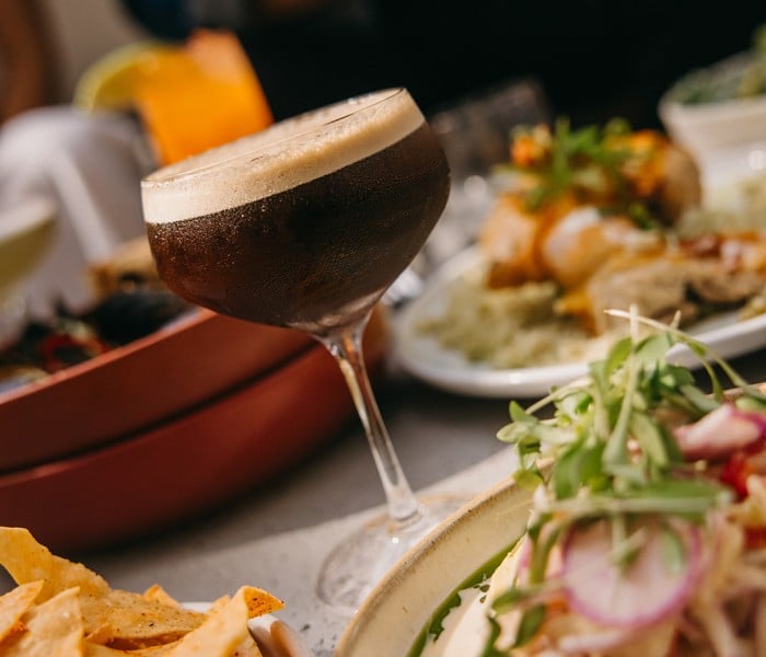 Dark beer in a stemmed glass with a foamy head at a shared meal, surrounded by chips and plates of food.